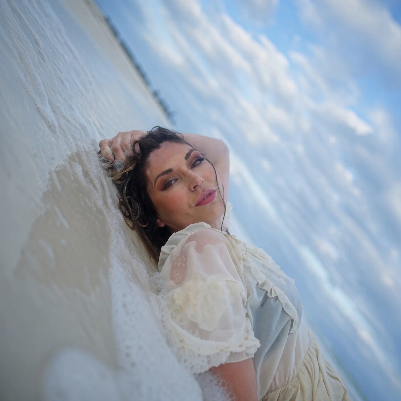Mujer con vestido blanco recostada en la orilla del mar en una playa de Cancún, México