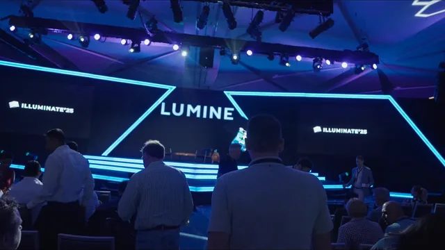 Audience before a stage with blue lights and the Lumine sign at the Inside Illuminate event