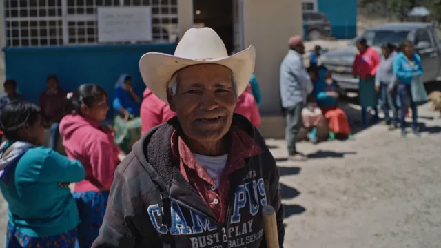Man in a white cowboy hat with people gathered behind him in a rural community in the Unidos Somos Maíz documentary
